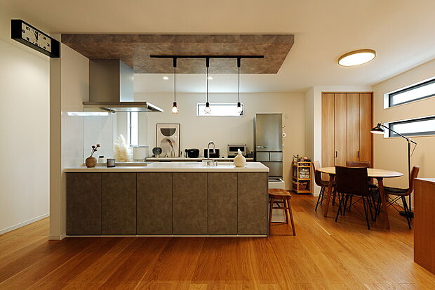 【当社施工事例】
リビング側のフロント部分が収納スペースになっているため、細々とした日用品もスッキリ。キッチンの上部は下がり天井にしてペンダントライト3つをリズミカルに設置し、空間のアクセントに。