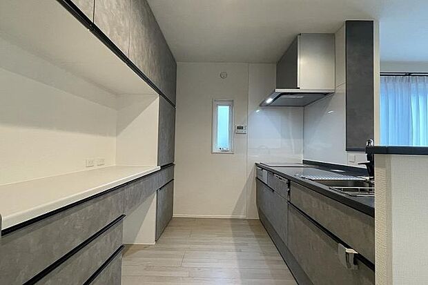 【No.1_キッチン（撮影_2025年10月）】グレー系で統一されたリビングダイニングを見渡せる対面式キッチン。