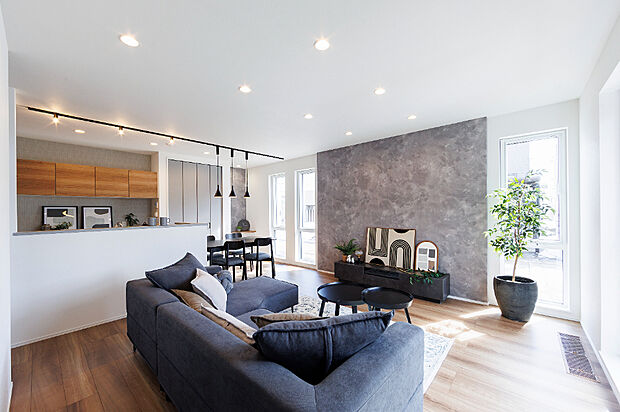 【【2号棟/リビング】】素材感のあるアクセントウォールが空間の印象を引き締めます。庭の緑を取り込む大きな窓が、日常に心地よい開放感をもたらすモダンな住まいです。(2026年3月撮影)