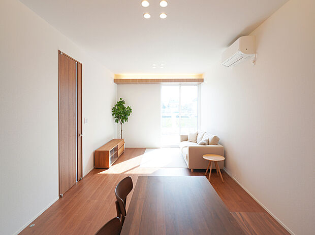 【Ｄ棟モデルハウス】18帖のLDKに大きな窓から光が広がり、下がり天井と高い天井が立体的な奥行きをつくる空間。間接照明とダウンライトが陰影を整え、家族が自然と集まる、上質で開放的なリビング