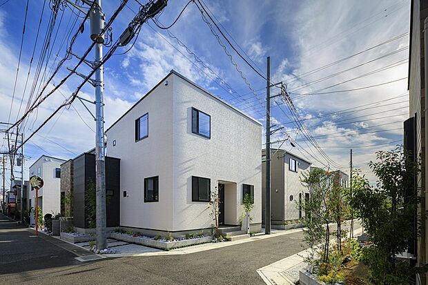 【【ナチュラルな表情の住まい】】白い外壁にブラックのサッシやロックガーデンデザインが映える住まいです。建物の両側にバイクスペースやカースペースを配置しています。/6号棟(2025年10月撮影)