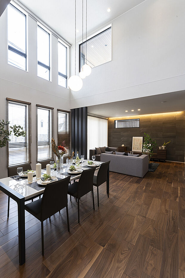 【【1階約29.8帖LDK/J号地モデルハウス】】吹抜け2階部分の3連窓より、陽光が注ぐリビング・ダイニング。濃い目のフロア材を施し、高級感のあるファミリースペースに仕上げています。29帖超の広々空間ですので、ご友人を招いてホームパーティも◎