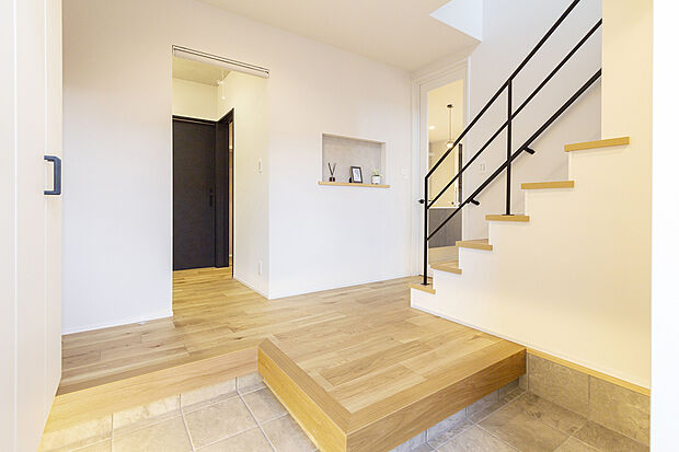 【住まいの顔に相応しい玄関ホール/B号地玄関ホール】アイアン手すりのオープン階段が目を引く、吹抜けのようは開放感あふれる玄関ホール。リビングへと続くガラス扉が空間にさらなる広がりと上質感をもたらします。大容量の土間収納やニッチなども。