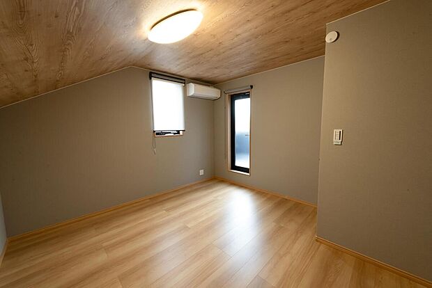 【【2階約7.5帖寝室/A号地モデルハウス】】アースカラー×木目クロスが落ち着いた雰囲気を演出!ゆったりとお過ごしいただける広さを確保しており、子育て中のご家庭など、ご家族揃ってお休みいただくこともできます。こちらからバルコニーに出入りできます。