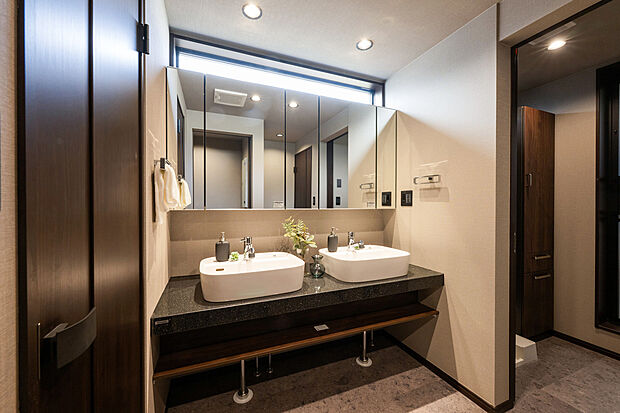 【A号棟：洗面化粧台】人造大理石のカウンターにダブルボウルを備えたフロートタイプの洗面台。大容量の五面鏡裏収納内部のコンセントは、電動歯ブラシや美容器具の充電にも。