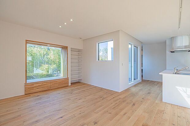 【4号棟】大きな窓から緑と空を望む心地よい空間。木の温もりを感じるベンチで、読書やコーヒータイムを楽しむ。自然と調和する、癒しのリビング。