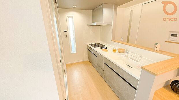 【【ondo建物プラン例/キッチン】】木目の床にグレーの面材が映えるキッチン。ゆったりとした天板と白のシンクが清潔感を演出し、窓からの光が柔らかく差し込む心地よい調理空間です。
