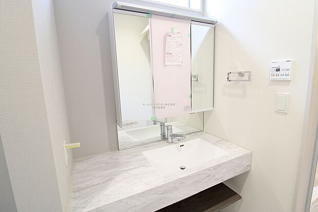 【洗面所】ワイドタイプの化粧台は、扉を付けない宙に浮かせたスタイル。石目や木調の落ち着いたテイストを組み合わせ、洗練された印象です。フルフラットのカウンターはお掃除ラクラク。デザインと機能性を両立しました。