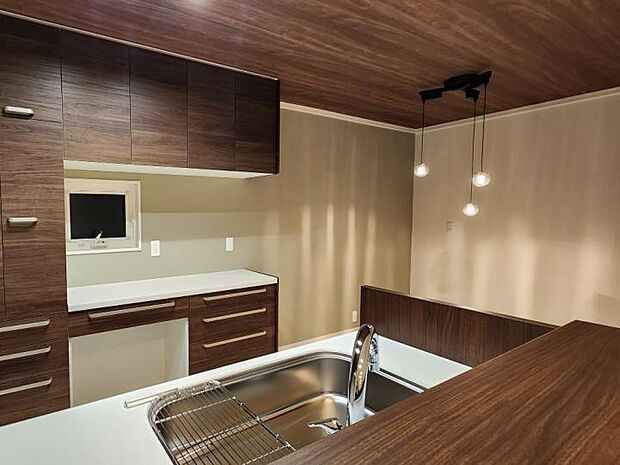 【B棟キッチン（2023年12月撮影）／】ダイニングキッチンは天井の壁紙は木目彫を。背面の壁紙は薄い緑色を採用し、自然の中にいるような空間を演出。