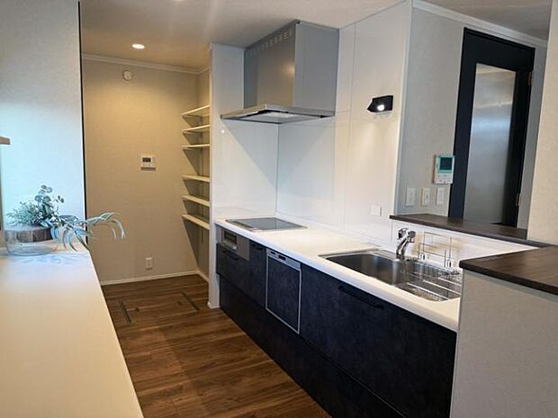 【D棟キッチン】モダンで機能的なキッチン。シンプルなデザインとダークカラーのキャビネットが特徴で、広々とした作業スペースと収納棚が備わっています。（2025年11月撮影）