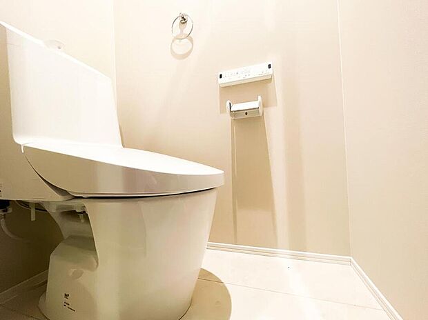 【トイレ】柔らかな色調のアクセントクロスが落ち着いた雰囲気を醸し出すトイレ空間。手洗い一体型のスタイリッシュな温水洗浄便座を採用しています。壁面にはタオルリングや便利なリモコンがスッキリと配置されています。