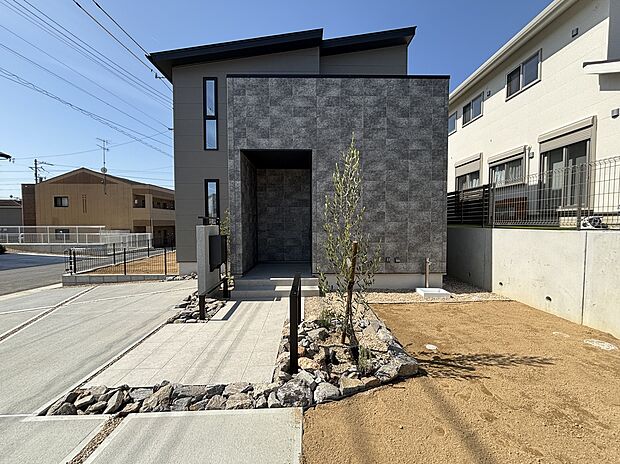 【洗練の東アプローチ】南道路物件ならではの陽当りと、東面に配したこだわりのアプローチ。大判タイル壁の重厚感と、ロックガーデンに立つ若木が調和した、モダンな外観デザインです。