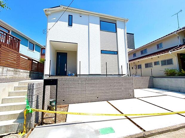 【現地外観写真】青空に映える、白を基調としたモダンな外観デザイン。広々とした駐車スペースは、ファミリーカーの駐車も楽々で、新しい暮らしを快適にサポートします。