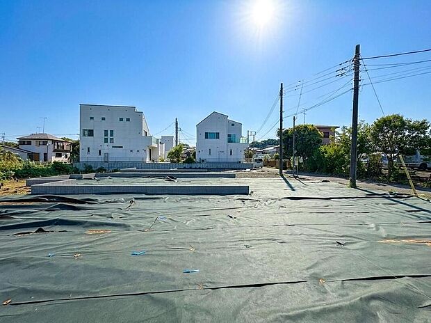 【現地外観写真】青空の下、陽光降り注ぐ広々とした区画。モダンな街並みが広がり、新しい家族の物語が始まる予感。子育て世代にぴったりの明るい住環境です。
