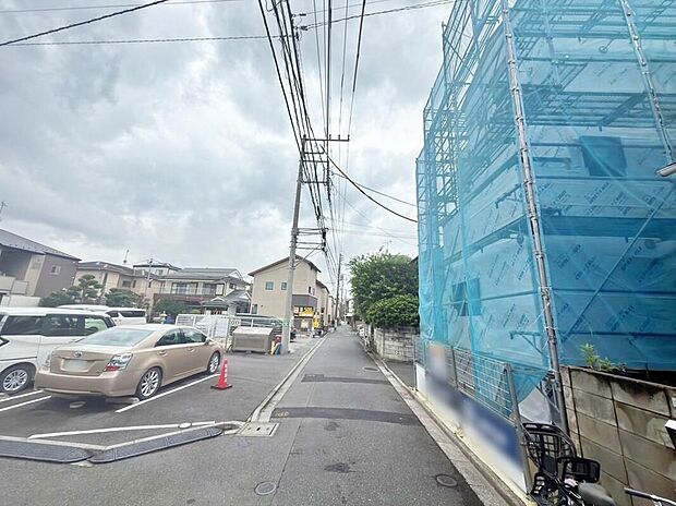 【前面道路含む現地写真】前面の舗装道路と電柱・電線、建築中の足場ネットが写っています。隣接に駐車場が見え、道路幅は約4mです。現地(2026年9月)撮影