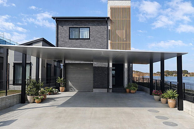 【施工例外観】大開口のカーポートが印象的な、重厚感あふれるモダン邸宅。縦格子がアクセントとなり、洗練された外観を演出します。ゆとりある駐車スペースと開放的な立地が、上質で快適な暮らしを実現します。
