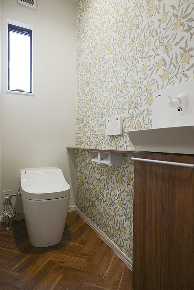 【1階トイレスペース】お手入れしやすいパナソニックのタンクレストイレ「アラウーノ」。 ボタニカル柄のアクセントクロスが目を引く清潔感ある空間です。