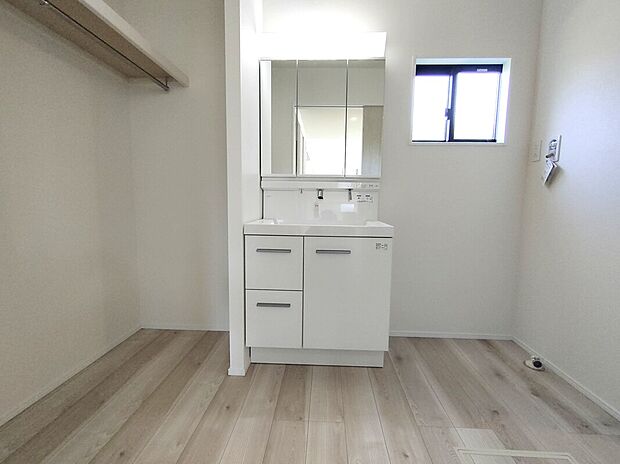 【洗面スペース(1号棟)】三面鏡収納付きの明るい洗面スペースに、タオルや日用品を置ける便利なラックをプラス。ハンガーパイプも備わり、身支度や家事がスムーズに進む使い勝手の良い空間です♪