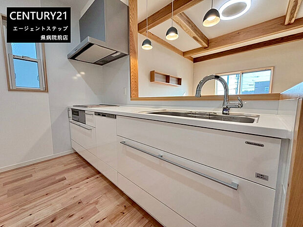 ホワイトを基調としたキッチンが空間に清潔感を与えています。天井の木目や梁がアクセントとなり明るい印象です。窓から自然光が差し込み開放的な雰囲気を演出しています。