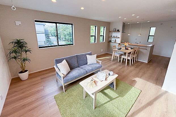 明るい陽射しが差し込むLDKは、家族との団らんにぴったり。ナチュラルな木目フローリングと開放的な対面キッチンで家事動線も良好。大きな窓から緑が見え、リビングで寛ぎながら四季を感じられます。(1号棟)