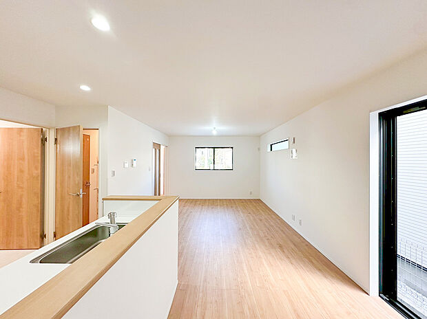 【リビング】南側に設けられた大きな窓と、奥のキッチン横の窓からたっぷりの陽光と心地よい風が流れ込みます。白を基調とした内装と明るい木目調のフローリングが、モダンで洗練された雰囲気を演出。