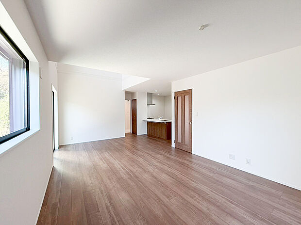 【リビング】温かみのある木目調のフロアと清潔感のある白い壁が、日々の生活を心地よく彩ります。キッチンとリビングが一体となった、使い勝手の良い理想の住空間です 。