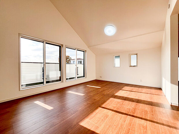 【リビング】陽光がたっぷりと降り注ぐリビングは、吹き抜けによる開放感あふれる高天井が魅力の空間です 。19帖超のゆとりある広さに加え、大きな窓から広がる空と、白を基調とした壁が明るく心地よい住空間を演出します 。