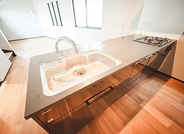 【システムキッチン】リビングに降り注ぐ明るい日差しがそのままキッチンにも柔らかく降り注ぐ明るい印象のキッチン廻り。リビングとキッチンの間に壁を設けてないフルオープンタイプですので、空間に一体感を感じられます。