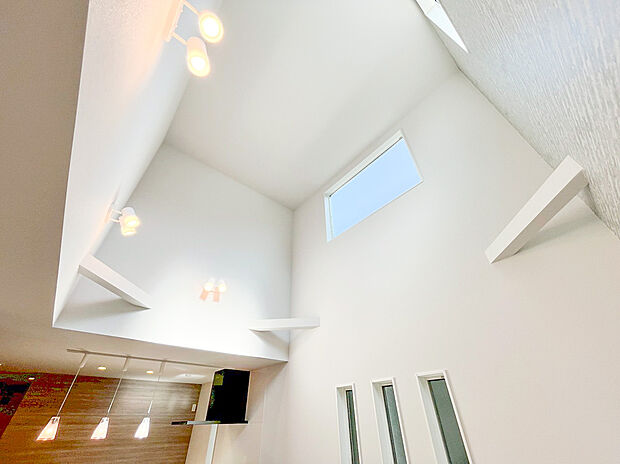 【リビング吹抜け】ダイナミックな吹き抜けが、圧倒的な開放感を演出！ 天井まで続くアクセントウォールが、空間に洗練された高級感を与えます。複数の窓から光が満ちる、明るく広々としたリビングです。