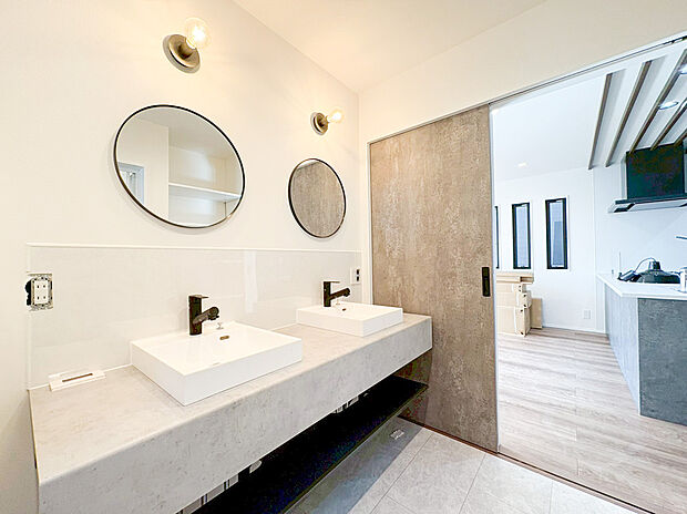 【造作ダブルボウル洗面台(アイカ製)】「忙しい朝も、二人並んで心地よく」 コンクリート調のカウンターに、マットブラックの水栓が映える洗練されたパウダールーム。 円形のミラーと温かみのあるブラケットライトが、毎日の身支度を特別な時間を演出。