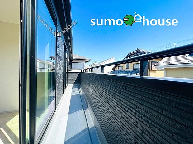 【落ち着いた住環境】空を身近に感じられる開放的なワイドバルコニーです。黒のシャープな手すりと壁面がモダンな印象を与え、室内に明るい陽光を呼び込みます。便利な物干し金物も完備し、家事動線にも配慮された心地よい屋外空間です。