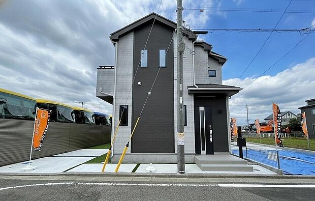 外観画像:落ち着いたツートンの外壁が映える角地の新築一戸建て。広めの駐車スペースと整った前面道路が毎日の出入りをスムーズにし、明るい空と調和するモダンな佇まいが暮らしにゆとりをもたらします。