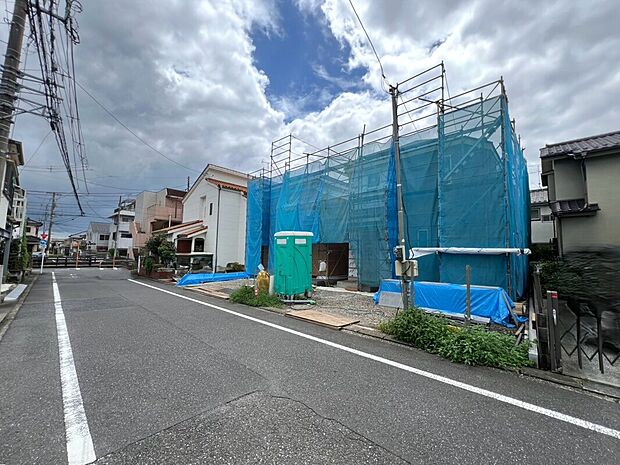【前面道路含む現地写真】1号棟 2号棟 前面道路は幅6mで車の出入りがしやすく、隣接する二階建て住宅と調和する街並み、青空の下で快適な住環境が感じられ、毎日の暮らしに安心感を添えます。