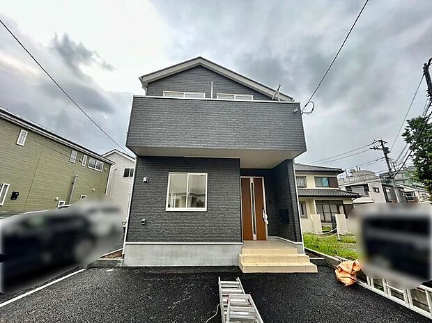 【現地外観写真】【1号棟】ダークグレーの洗練された外観が目を引く、モダンな佇まいの一戸建てです。広々とした駐車スペースは、家族の車を停めるだけでなく、お子様との遊び場としても活用できます。