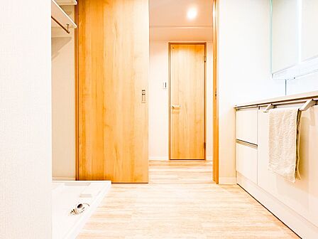 洗面室から浴室まで一直線に繋がる、使い勝手の良い機能的な動線。明るい木目調のフロアが、水回り特有の冷たさを感じさせず、温かみのある空間を演出します。毎日の家事がスムーズに捗る、暮らしに優しい設計。