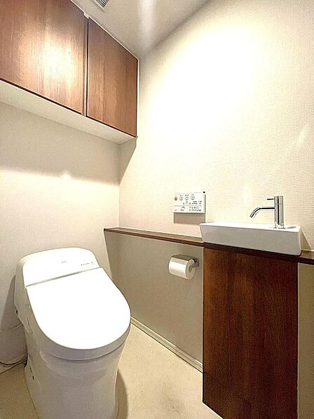 木目調の収納と手洗い器がスタイリッシュなトイレ空間。温水洗浄便座で快適、上部収納でストックもすっきり片付き、いつも清潔に保てます。