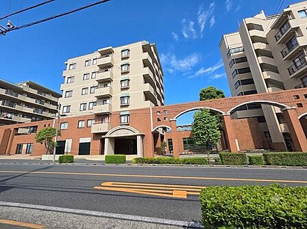 重厚感のあるタイル貼りの外観とアーチ形のエントランスが印象的なマンションです。手入れの行き届いた植栽が街並みに彩りを添え、ゆとりある敷地計画が落ち着いた住環境を演出します。
