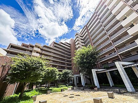 青空の下、緑豊かな広場が広がるマンション外観。お子様がのびのびと遊べるスペースがあり、家族の笑顔が溢れる毎日を育みます。