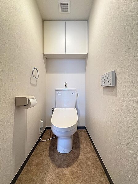 白を基調とした清潔感あふれるレストルーム！上部にはトイレットペーパーや清掃用品をすっきりと隠して収納できる便利な吊戸棚を完備。温水洗浄便座付きで、毎日快適にお使いいただけます。