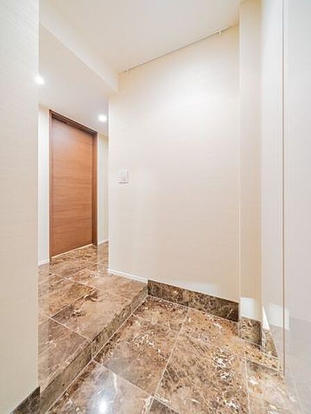 【玄関】玄関から廊下までの床部分は、華やかな天然石を用いた仕様となっています。トールタイプで収納力のあるシューズボックスが設置されています。