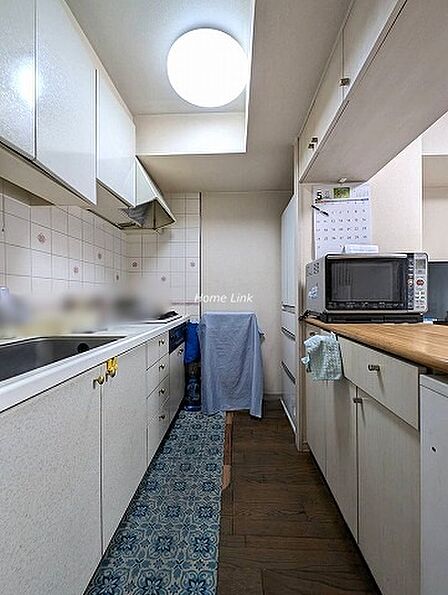 【キッチン】左側にシステムキッチン、右側に対面カウンター、奥に冷蔵庫の配置です。対面カウンターの上下は収納スペースになっており食器棚を置く必要はありません。