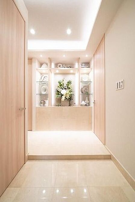 光沢感のあるタイル床と木目調の建具で仕上げられた玄関スペースには、折り上げ天井やダウンライトに加え、正面の壁面に照明付きの固定棚が備え付けられています。