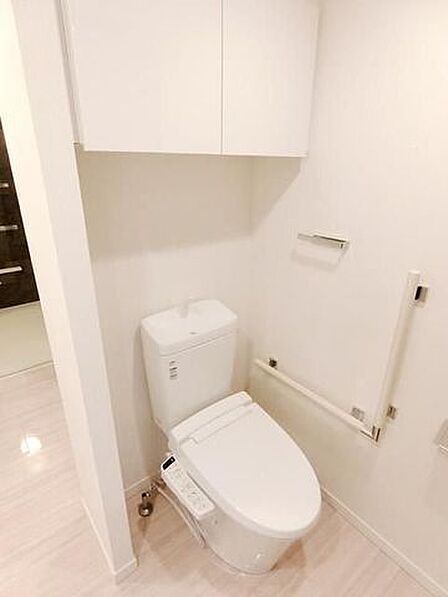 白を基調とした清潔感のあるトイレには、温水洗浄便座機能を備えた便器に加え、立ち座りをサポートする手すりや、トイレットペーパーなどの備品をすっきりと収納できる便利な上部吊戸棚が設置されています。