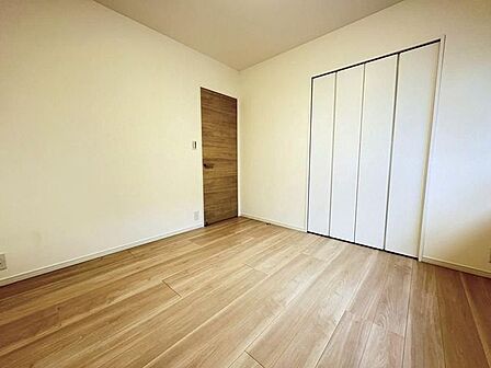 ナチュラルな木目調のフローリングと白いクロスで仕上げられた洋室には、木目調の出入口ドアに加え、壁面には白い折れ戸タイプの作り付け収納が備え付けられています。