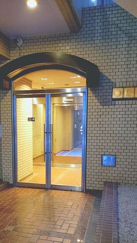 外壁やアプローチの床面はタイル貼りで仕上げられており、アーチ状の庇があるエントランスにはステンレス枠のガラス扉とダウンライトが配置されています。