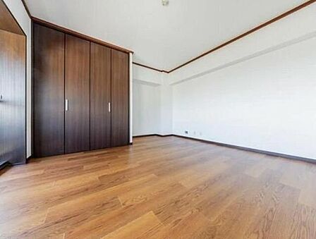 温かみのある木目調のフローリングと白いクロスで仕上げられた室内には、壁面にダークブラウンの大型クローゼットが備え付けられており、衣類や小物をすっきりと収納できます。