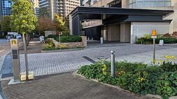 大きな庇が備えられた車寄せのアプローチ部分には石畳風の舗装が施されており、周囲には整えられた植栽が配置されています。敷地入口には照明設備や案内用のポールなどが設置されている設計です。