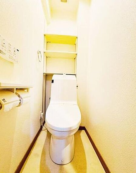 白を基調とした清潔感のあるトイレには、便器背面に使い勝手の良い作り付けのオープンラックが備わっており、壁面には2連式のペーパーホルダーやタオル掛け、温水洗浄便座用の壁掛けリモコンが設置されています。