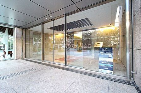 ガラス張りの自動ドアを採用したエントランスは、壁面や床面に石目調の素材が使用されており、天井にはダウンライトが設置されているほか、入口の奥にはオートロックの操作盤や点字ブロックが備え付けられています。