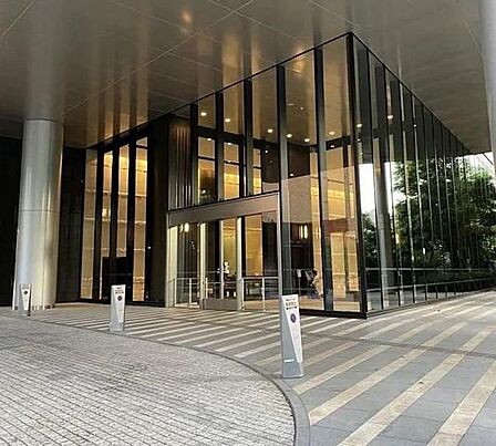 大きなガラス壁と高い天井が特徴的なエントランスには、ガラス製の自動ドアや円柱が配されており、アプローチ部分にはストライプ模様の敷石が綺麗に敷き詰められたデザインになっています。